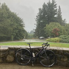 A bicycle leans against a low stone wall in the foreground. Somewhere in the distance, behind a thick veil of rain, is Mt. Hood.