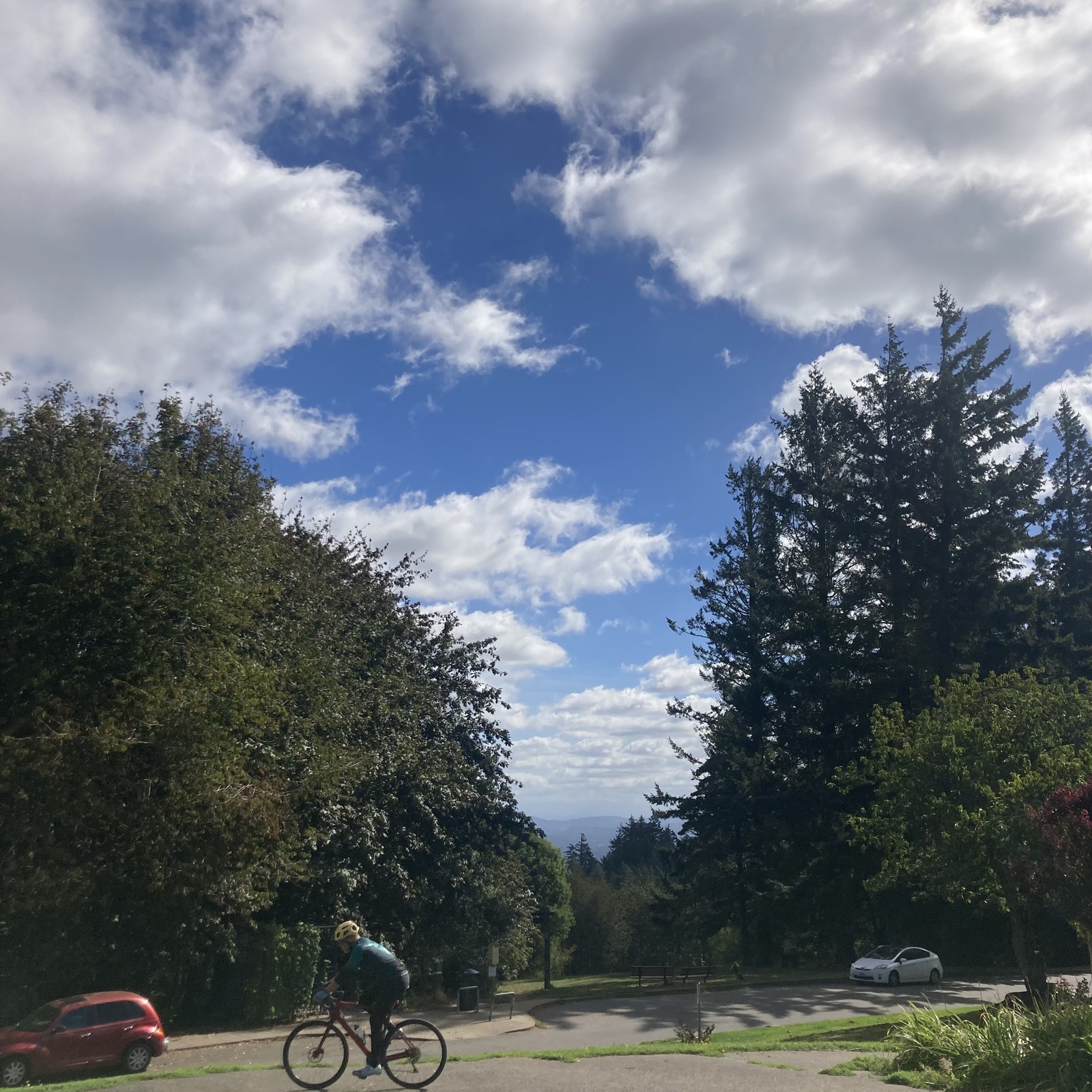 A cyclist rides past a brilliant cloudscape of broken fluffy white clouds under a deep blue sky.