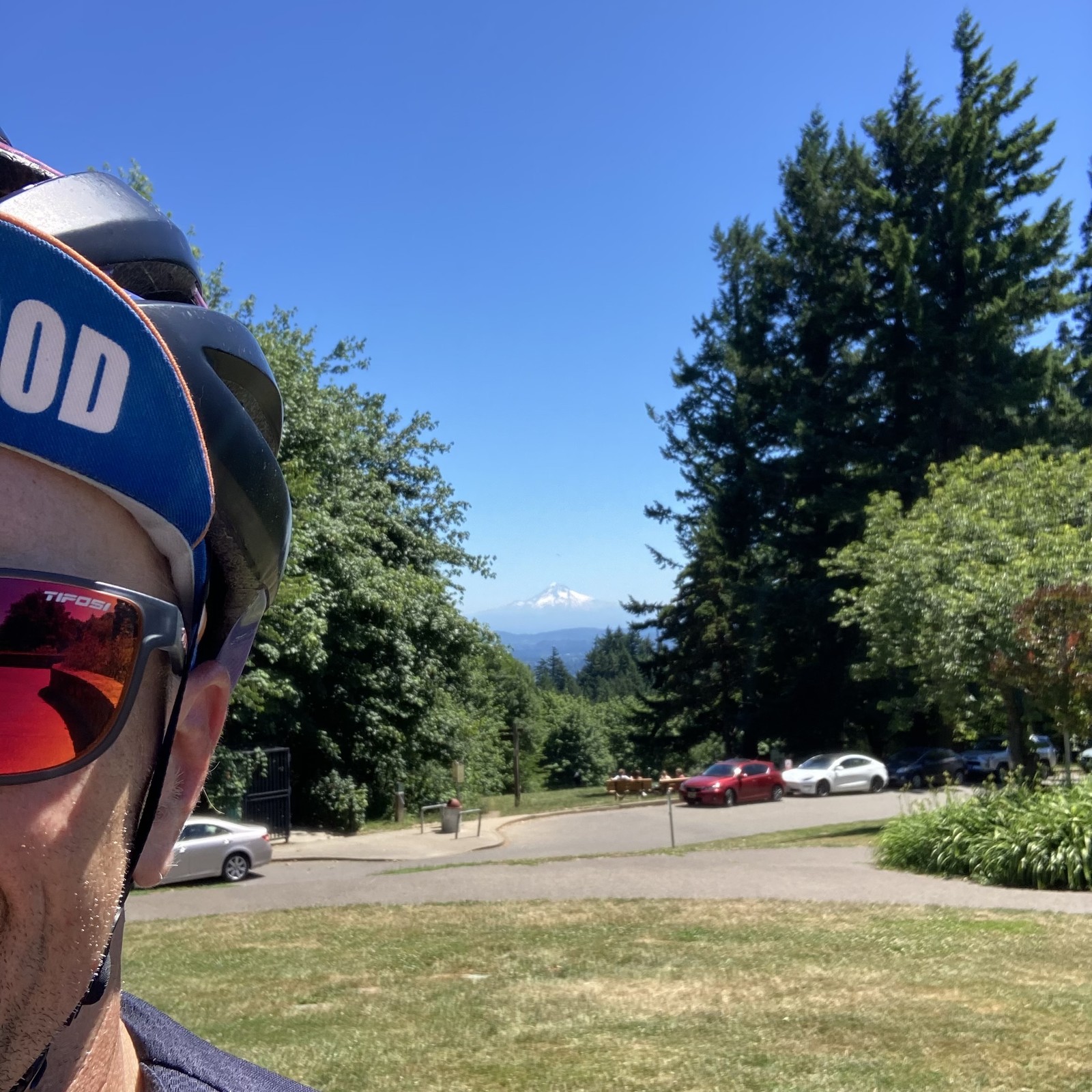 Selfie taken in front of Mt. Hood on a CRYSTAL clear day at solar noon. Only part of my face is visible in the foreground, I am wearing reflective sunglasses and a bicycle cap that reads “Sellwood”