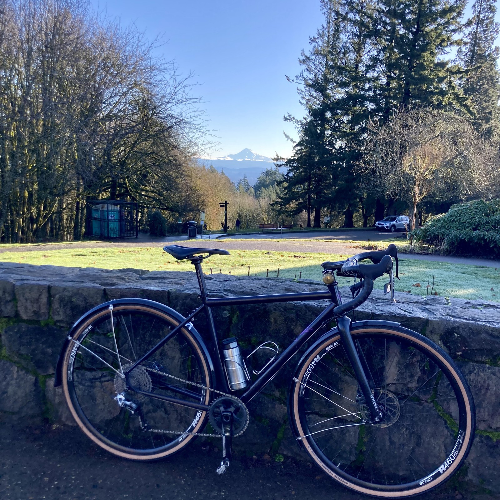 Mid-morning, early winter. Clear blue sky overhead. A shiny bicycle leans against a low stone wall in the foreground. A few wisps of low cloud cling to the foot of a lone snowy volcanic cone in the distance.