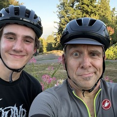 Father and son wearing quizzical expressions and bicycle helmets, Mt. Hood in the hazy background