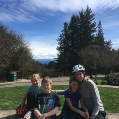 Three children and a woman seated on a low stone decorative wall at Council Crest Park, facing west toward Mt. Hood, which is not visible. The kids all look tired and grumpy.