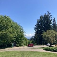 Mt. Hood under a deep blue sky, a few small white clouds clinging to its face and east side. Park is still and empty; a bright red SUV is parked about 50' away downhill