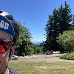 Selfie taken in front of Mt. Hood on a CRYSTAL clear day at solar noon. Only part of my face is visible in the foreground, I am wearing reflective sunglasses and a bicycle cap that reads “Sellwood”