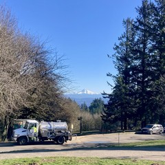 Mountain is bright with snow against a cloudless winter sky. In the middle distance a truck labeled “1-800-TOILETS” services a portapotty