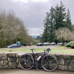 A bike leans against a low stone wall in a park at the top of a hill. Low clouds fill the sky and obscure the horizon